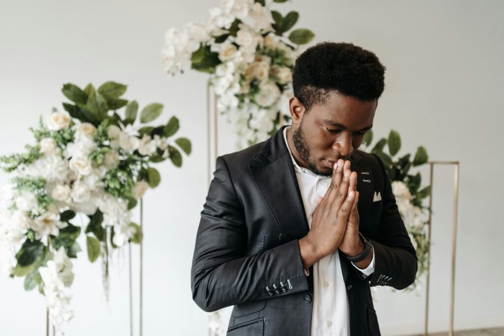 A contemplative man in a suit prays with hands together, surrounded by beautiful floral decor.