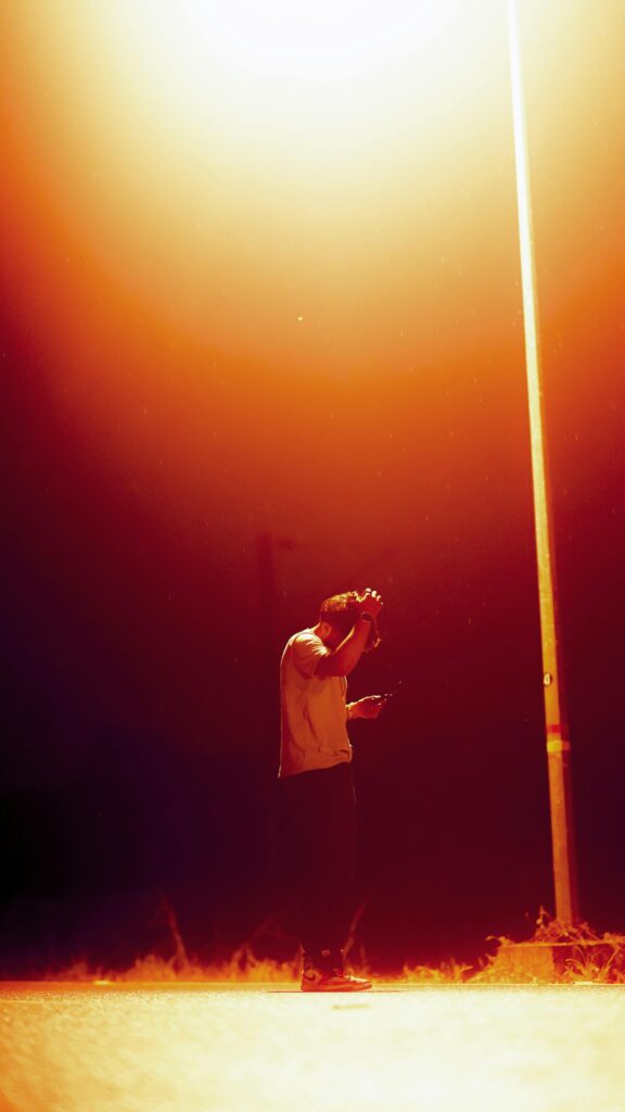A man stands under a streetlight at night casting a warm glow on the deserted road.