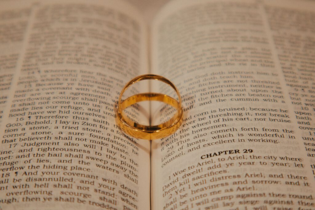 A gold wedding ring casting a heart-shaped shadow on an open Bible page symbolizing love and faith.