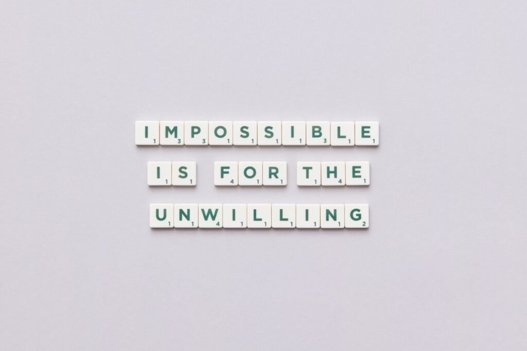 Inspirational quote 'Impossible is for the unwilling' made with letter tiles on a minimalist background.